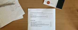 A top down photo looking at a desk with a set of paper on it - in focus is a printed copy of the safeguarding policy