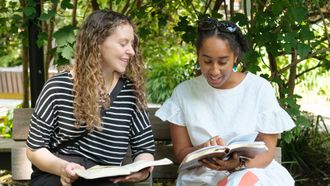 Two people sitting at a park bench, they both have a bible open in front of them