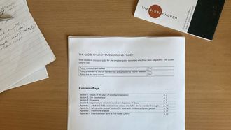 A top down photo looking at a desk with a set of paper on it - in focus is a printed copy of the safeguarding policy