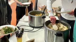 A table with two pots of food on it. Hands are serving food from the pots.