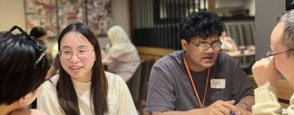 Four people sit around a table in conversation with one another.